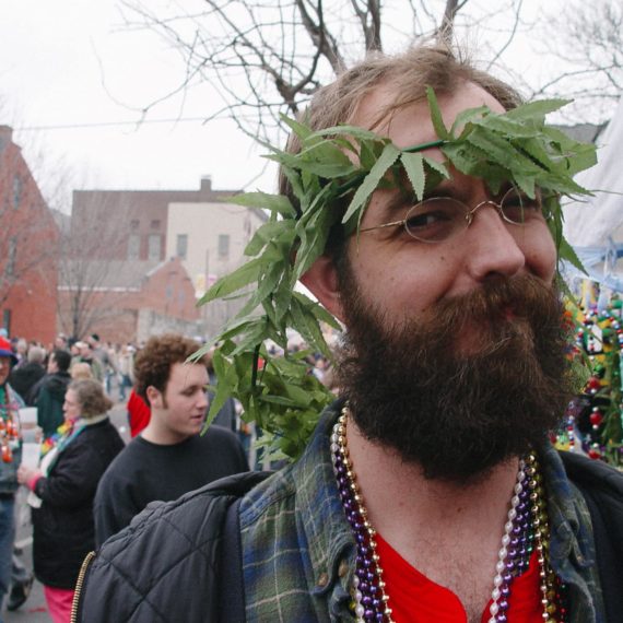 A bearded man with a crown of fake weed and Mardi Gras beads