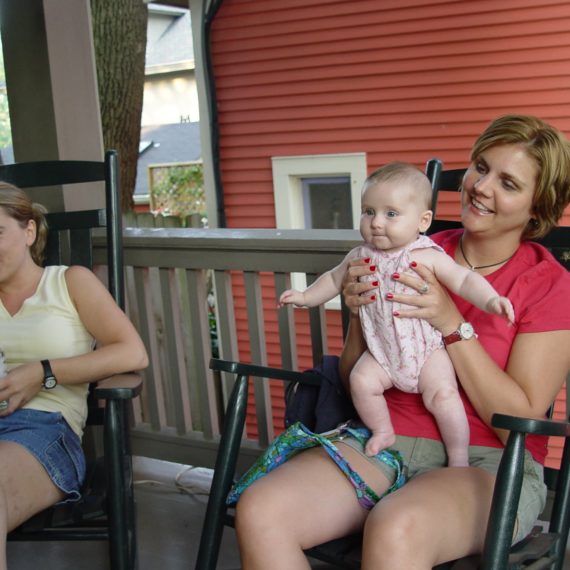 A woman in a rocking chair on a porch holds a baby