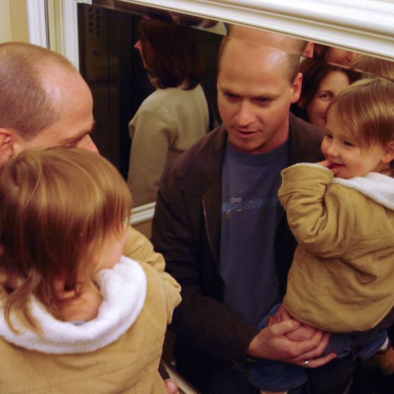 Parents in an elevator with mirrors and their toddler