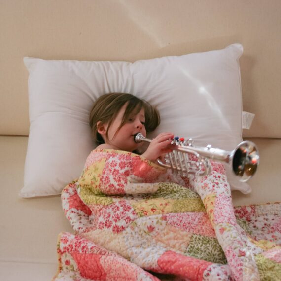 Young person playing trumpet under a quilt