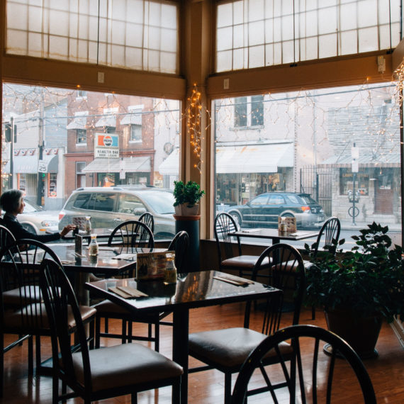 An Asian woman sits alone at a table in a restaurant staring out the window