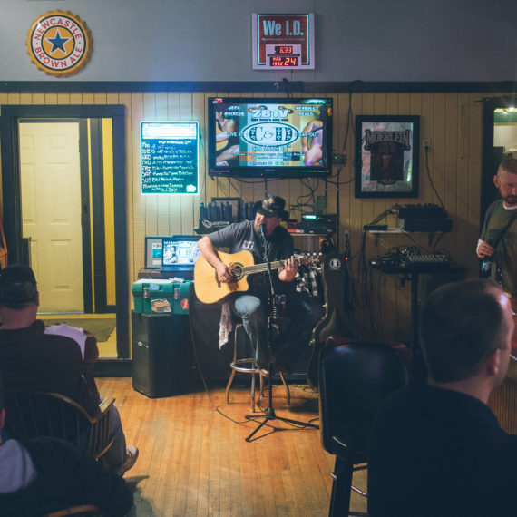 A man with an acoustic guitar singing into a microphone at a bar