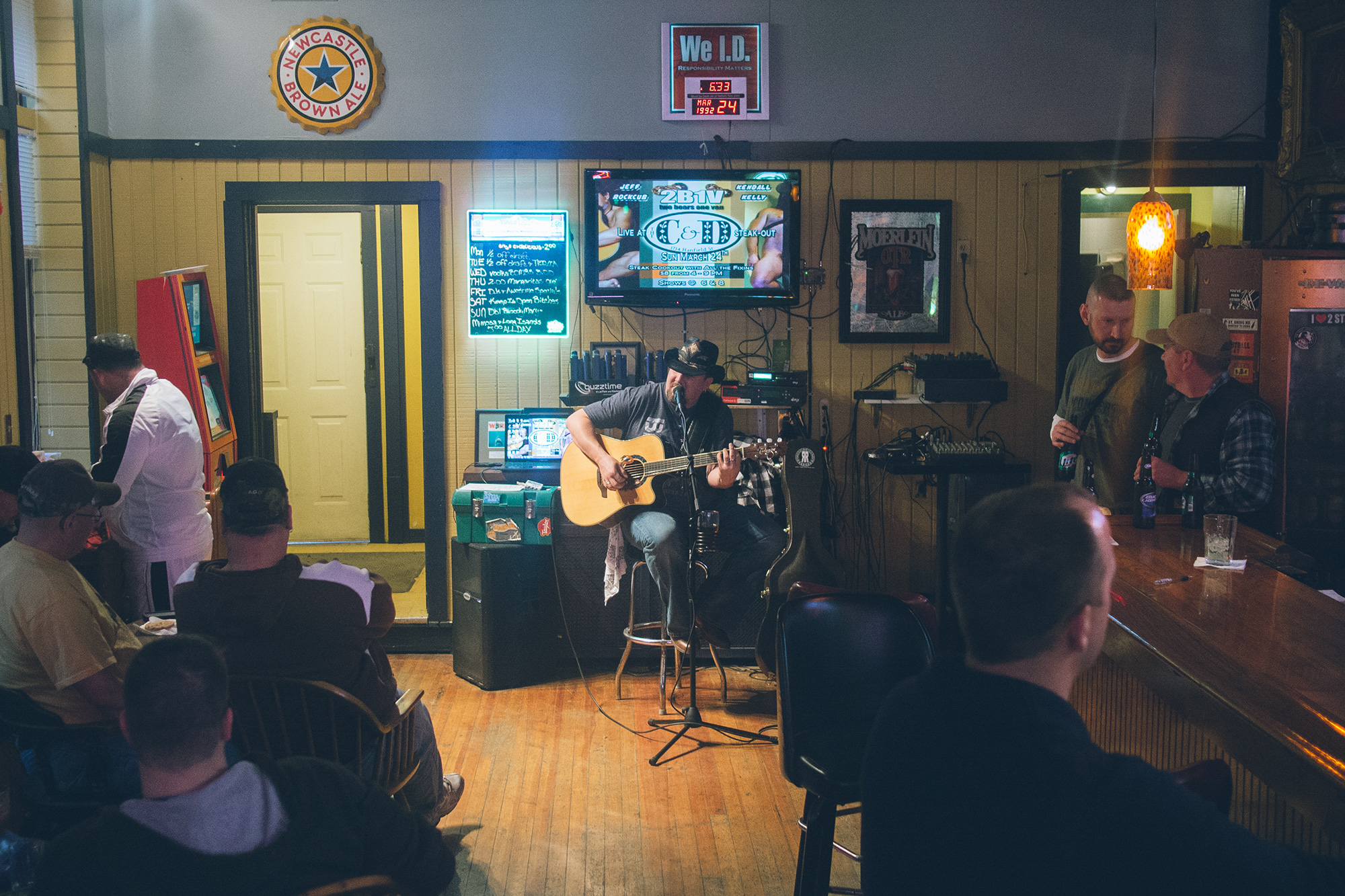 A man with an acoustic guitar singing into a microphone at a bar