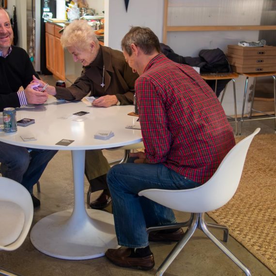 Three folks around a table playing Cards Against Humanity and laughing