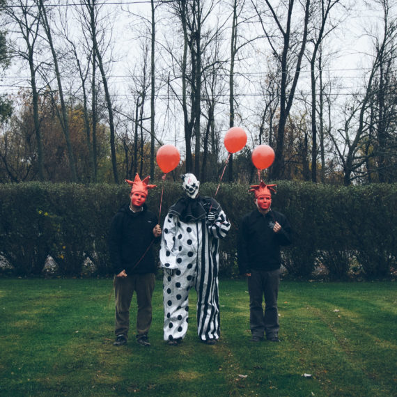 Two men in red masks flank a clown