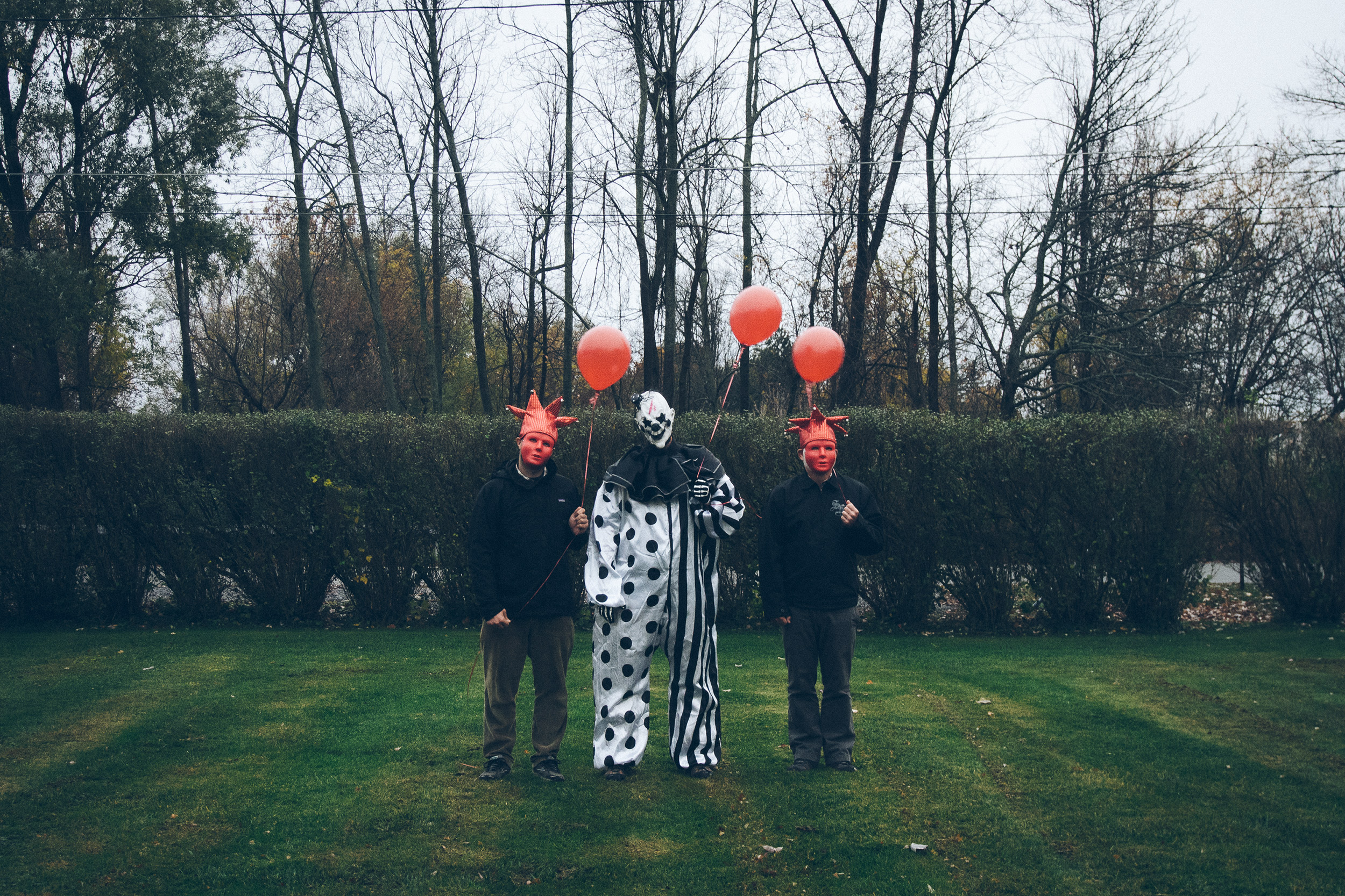 Two men in red masks flank a clown