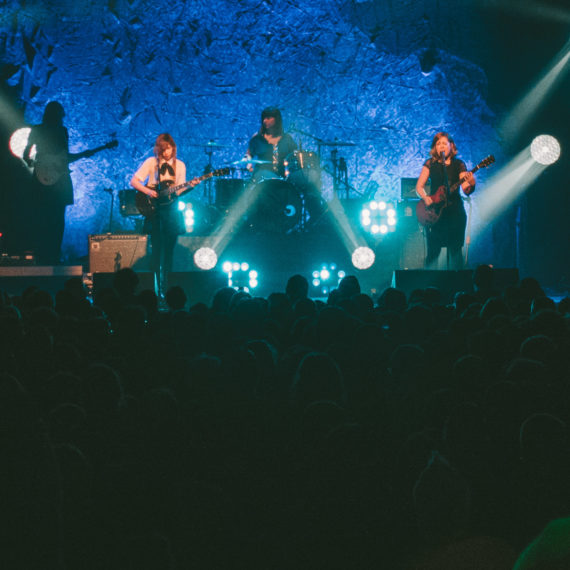 A rock band performs onstage amidst fog machines and blue lights