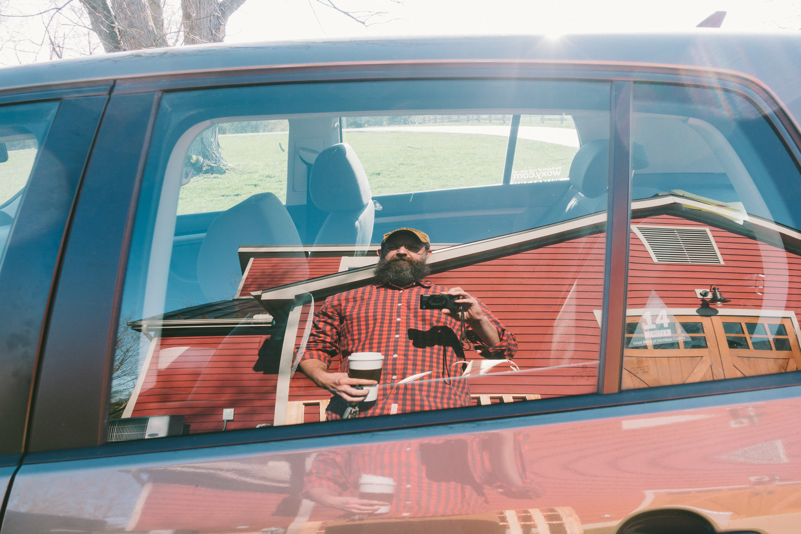 A man taking a selfie in the reflection of a car window