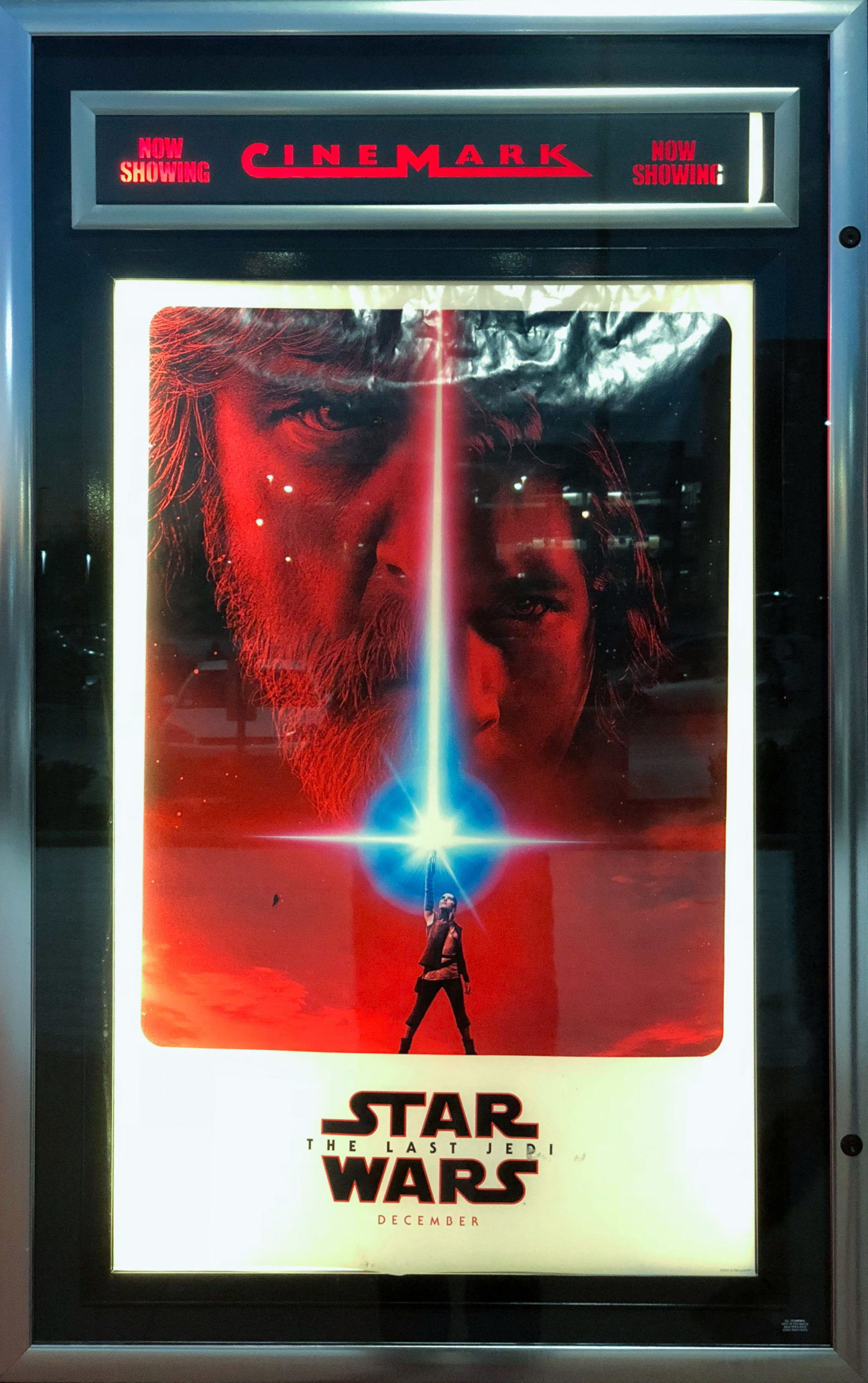 A poster for Star Wars, The Last Jedi with Rey wielding a blue lightsaber against a red photograph of Luke Skywalker and Kylo Ren