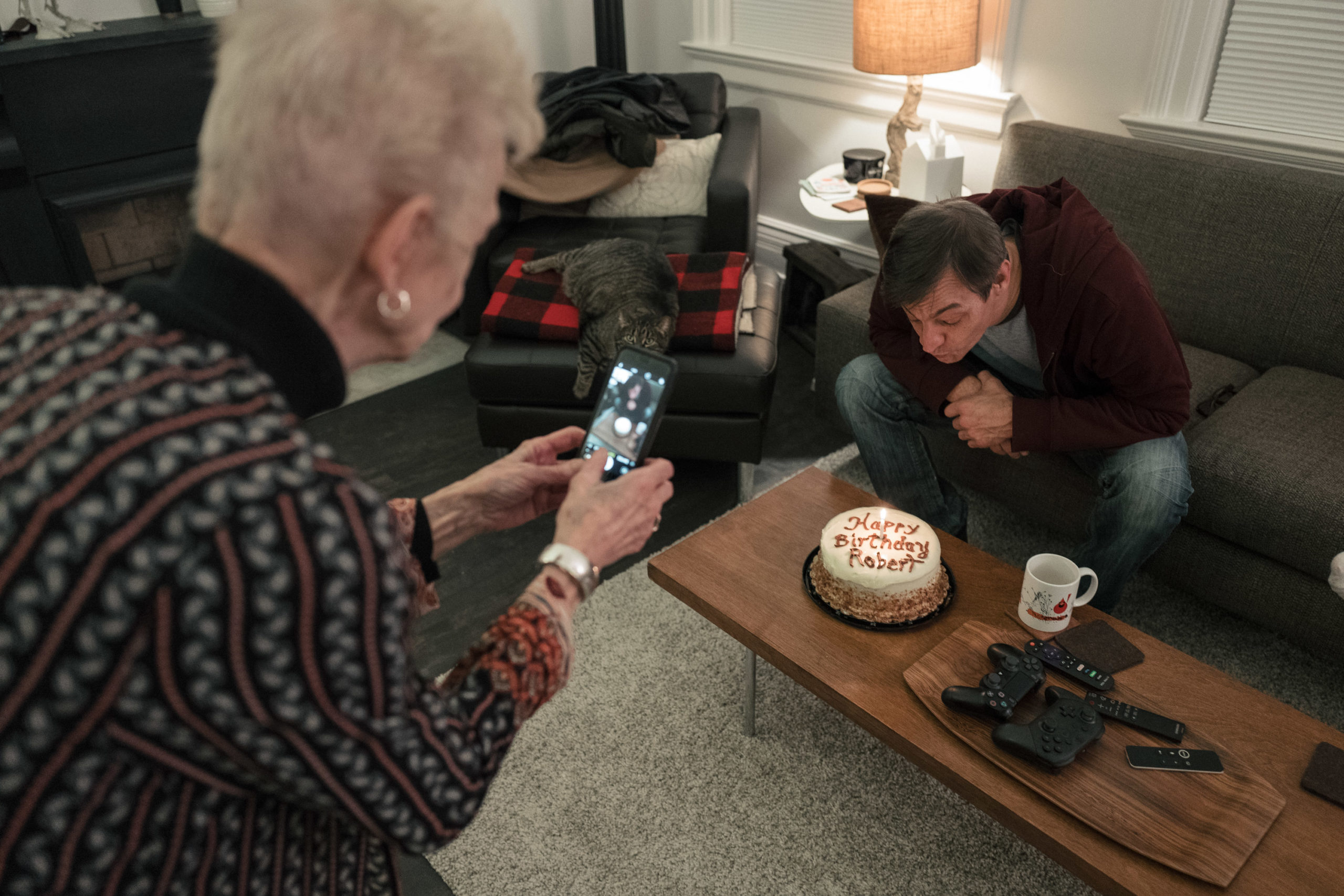 A woman taking a photo of a man blowing out birthday candles