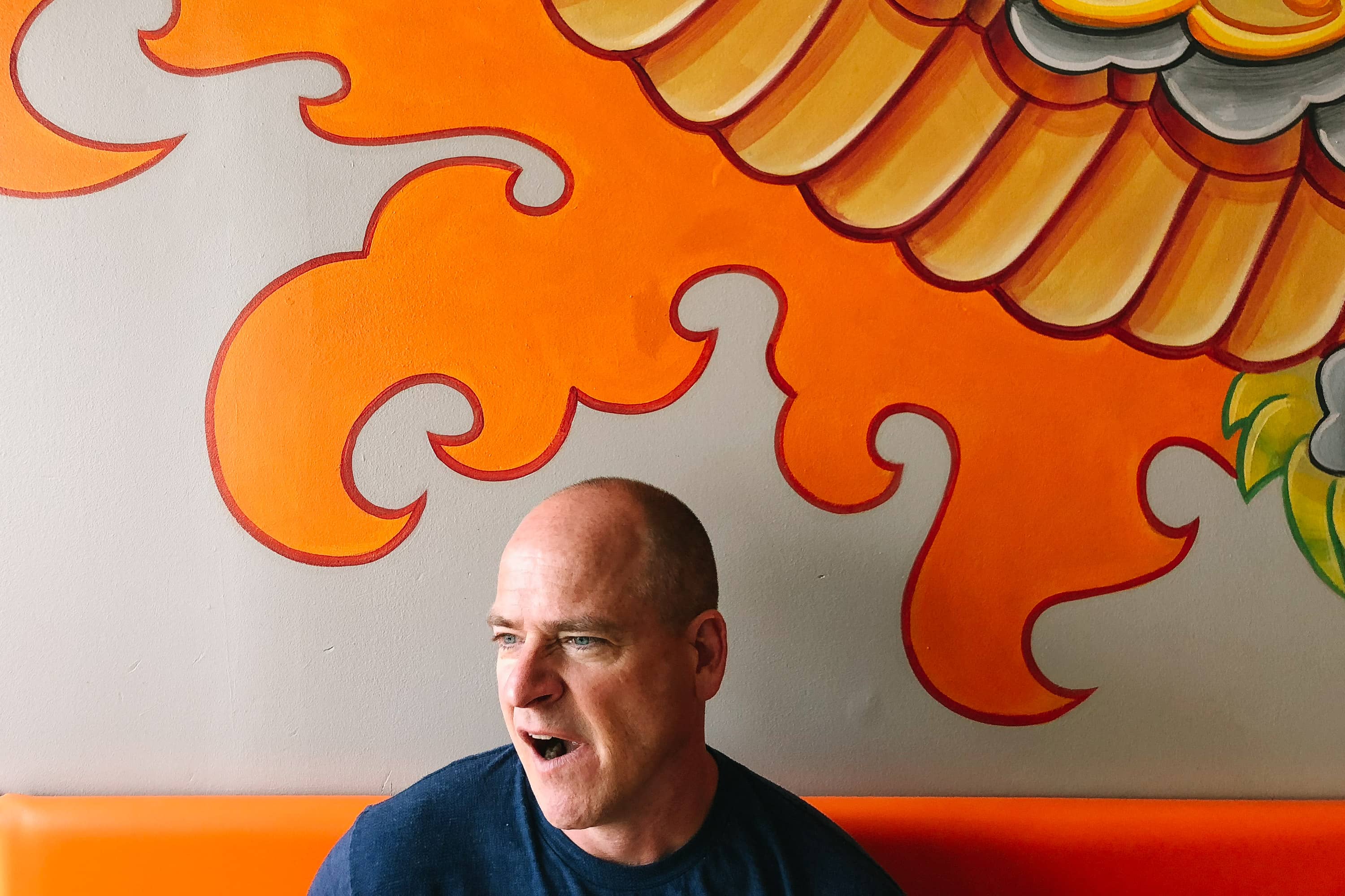 A man yawns in front of a mural inside a restaurant