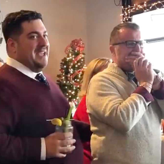 Holiday decorations surround two men at a proposal surprise party.