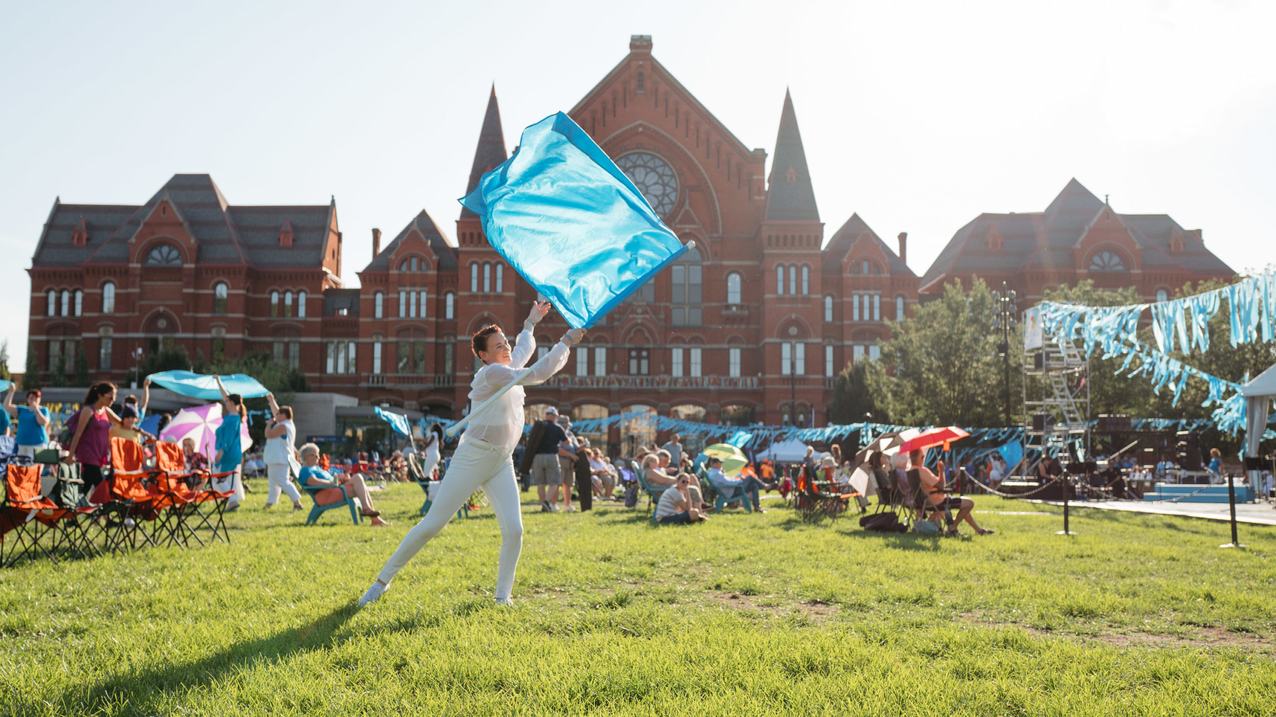 A figure in all white twirls a blue flag in front of an ornate building