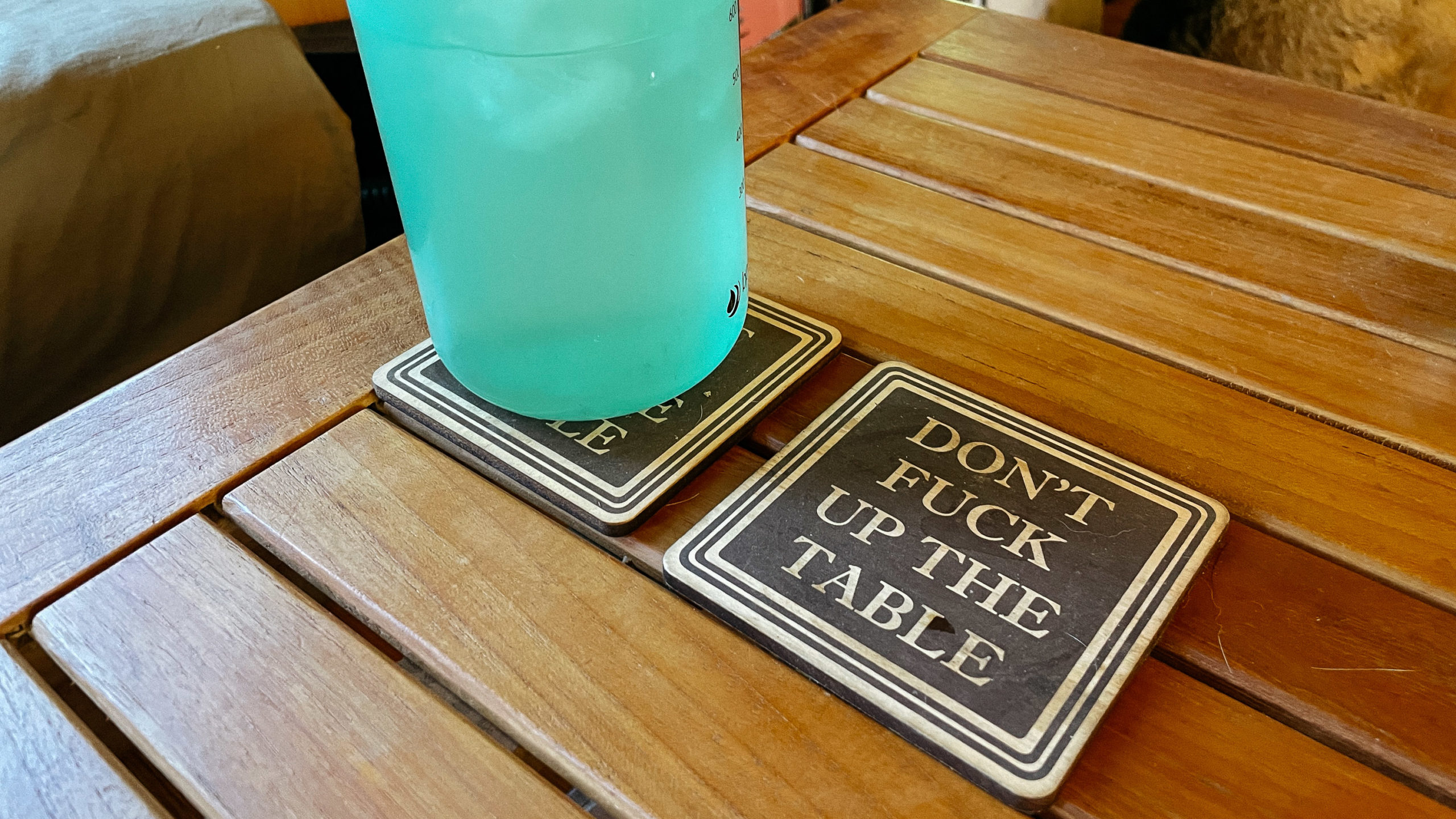 A funny coaster that reads "Don't fuck up the coffee table"