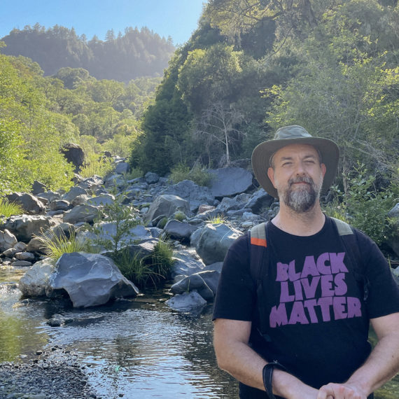 A man in a Black Lives Matter shirt with a hat in a rocky creek bed