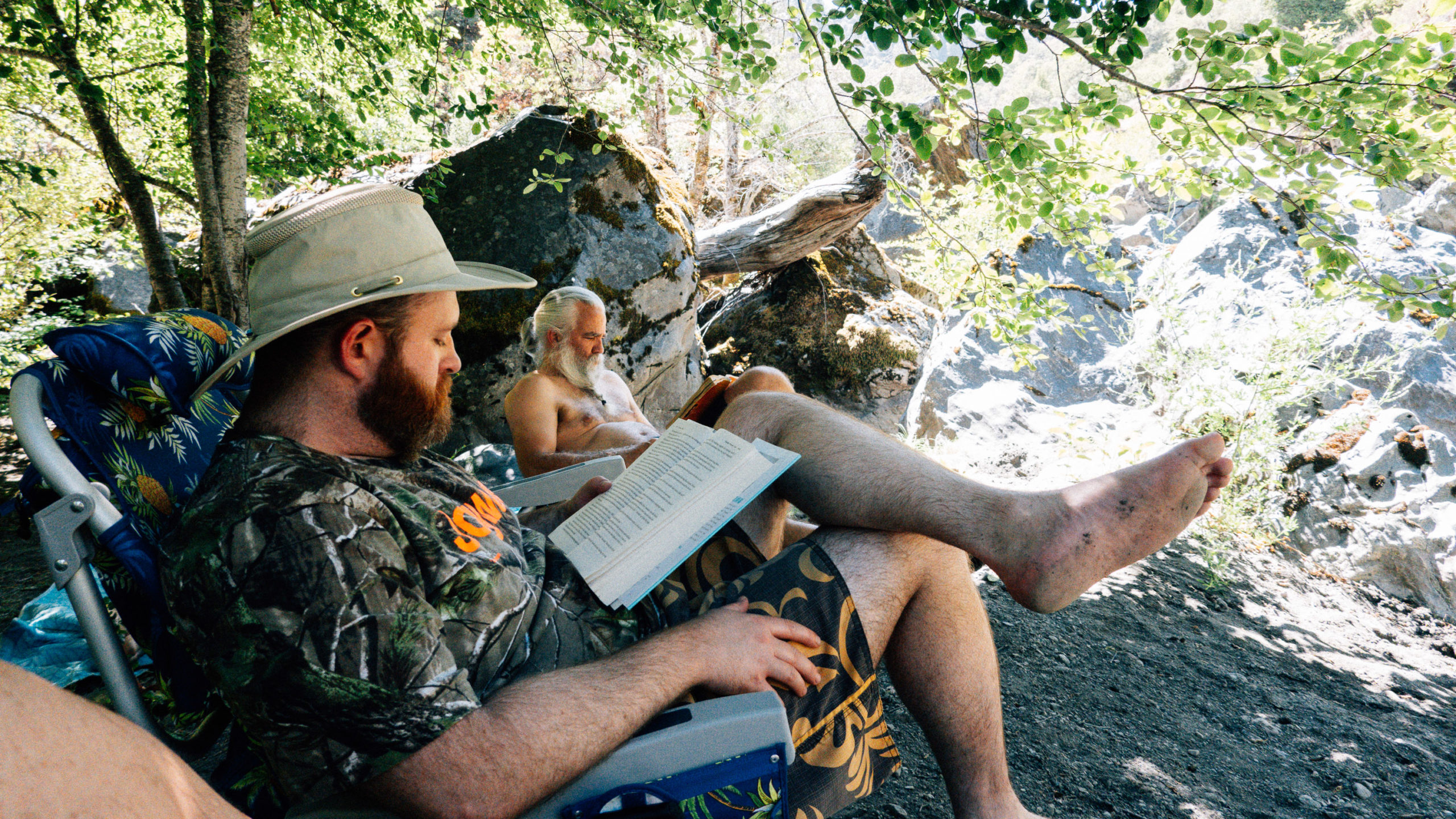 Bearded men reading in the shade at the side of the creek