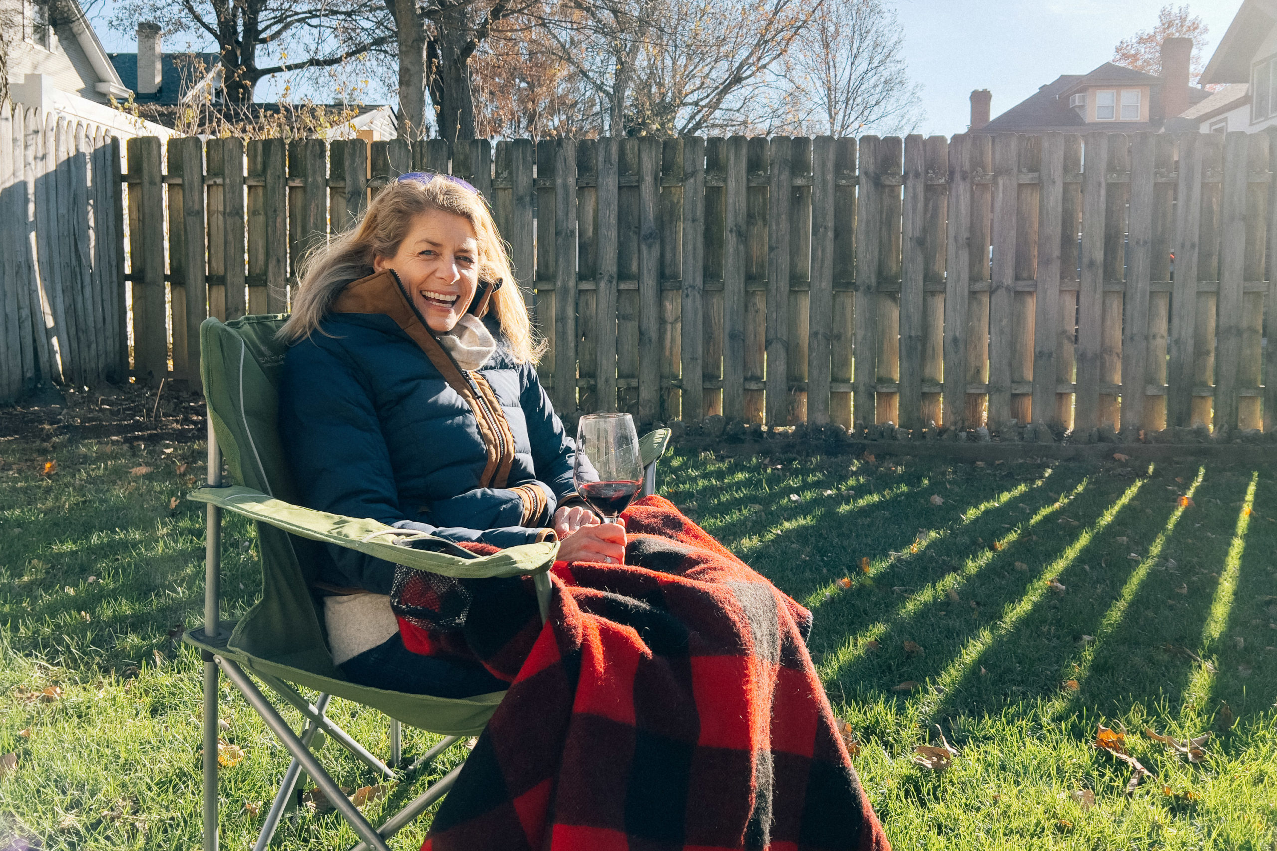 A woman sits in a camping chair with a lap blanket and glass of wine