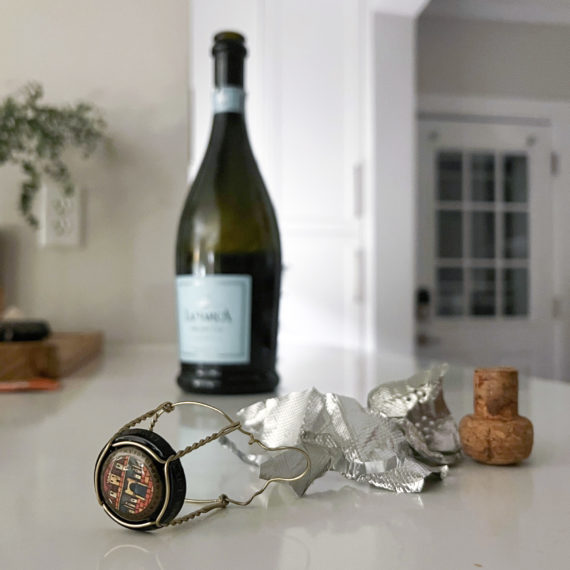 A bottle of prosecco with the cork off on a white countertop