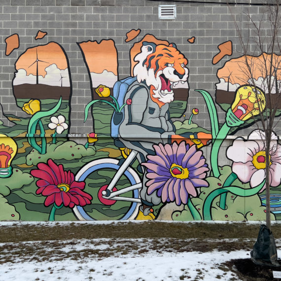 A spray painted mural on a cement brick wall of a tiger riding a bike