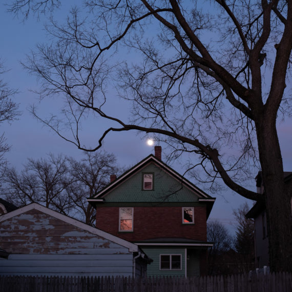 A garage, house, moon and tree at dusk