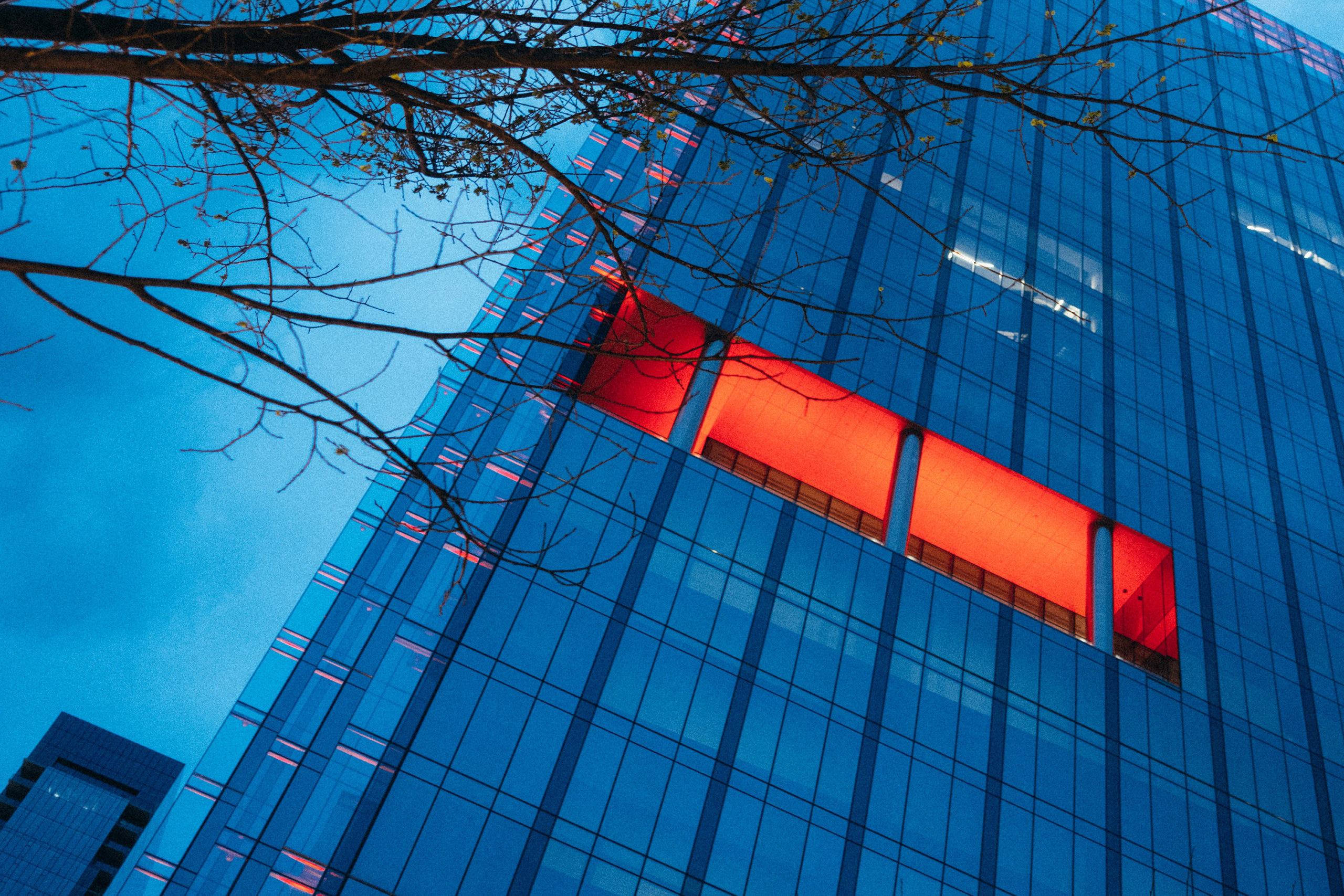 A blue skyscraper with an open section with red lighting