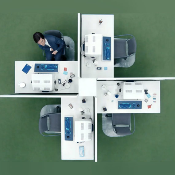 An overhead shot of four office desks arranged in a pinwheel on green carpet