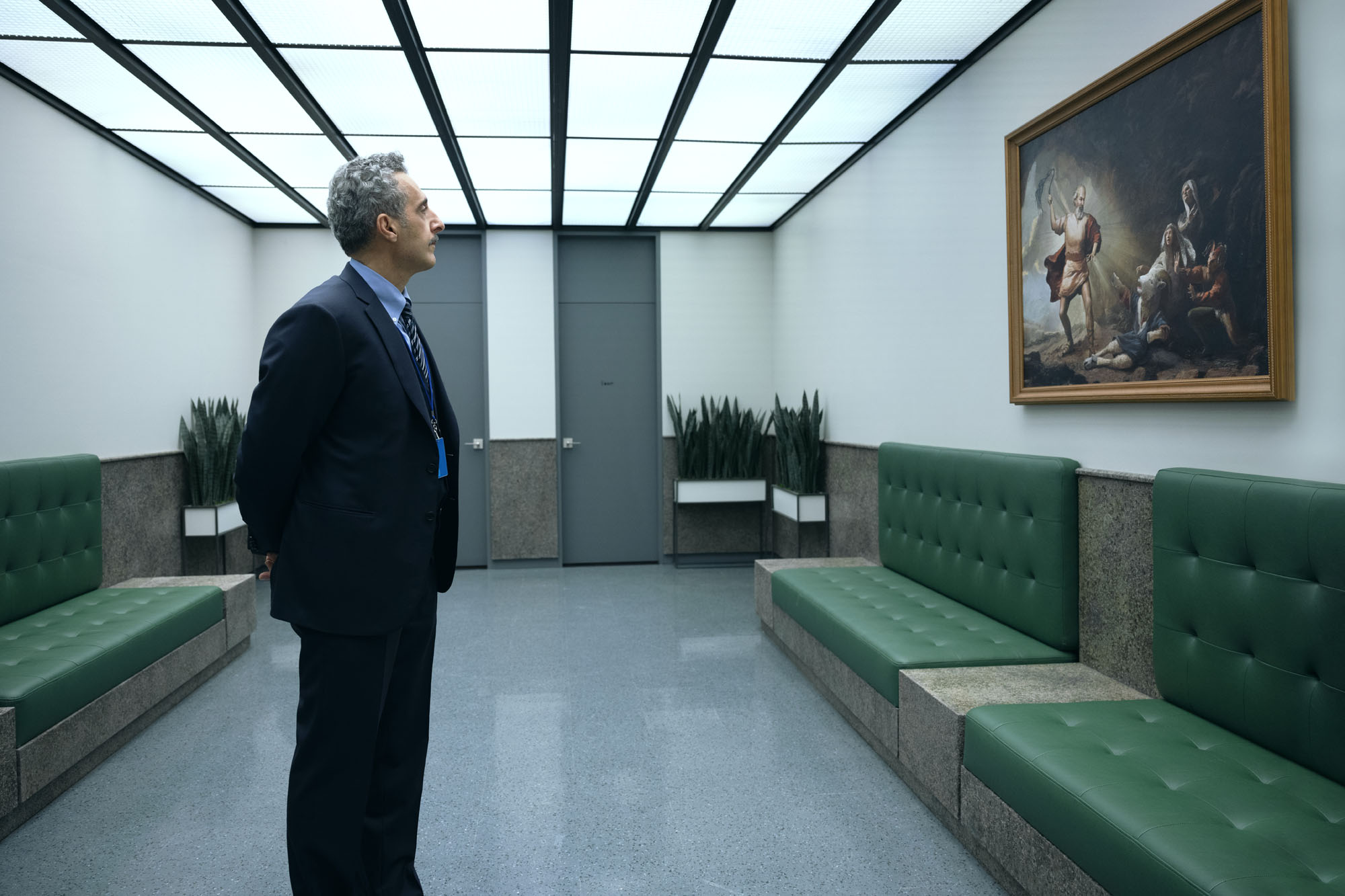 A man with a mustache regards a painting in a corporate room with lots of fluorescent lighting