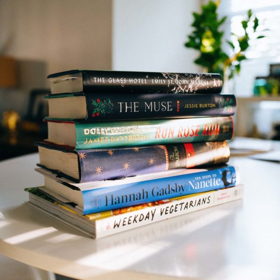 A stack of books dappled in sunlight on a white table