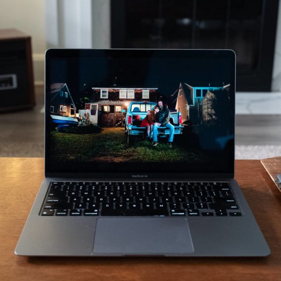 A laptop playing a movie on a wooden coffee table. In this scene a father and daughter sit on the back of a pickup truck at night. His arm around her as she leans in, about to leave for college the next day.