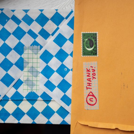 blue and white checked paper with gridded tape. A manilla envelope with a stamp with a bird and the letter C. More gridded tape with a bird face and the words Thank You!