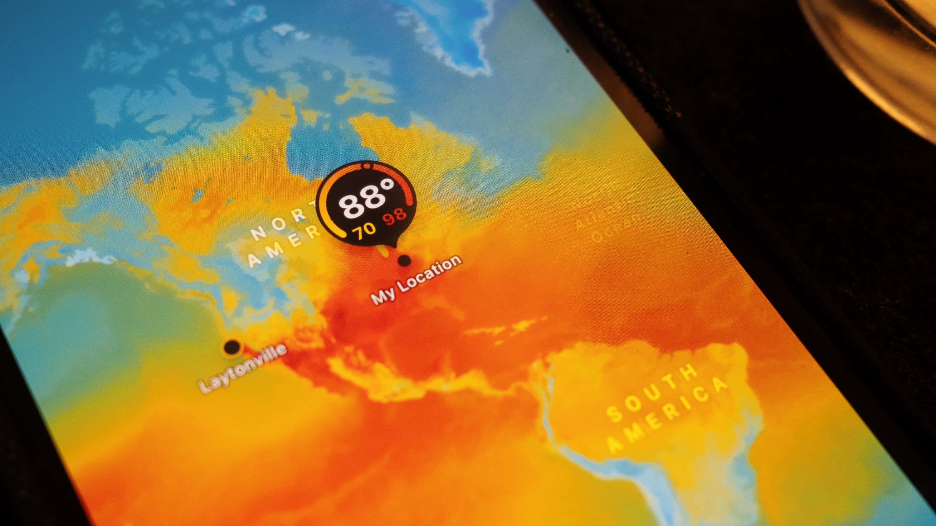 A photograph of a weather app on a mobile device showing a large red swath of high temperatures encircling earth