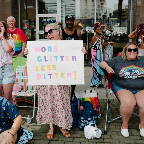 A woman holds a sign that reads "More glitter, less bitter"