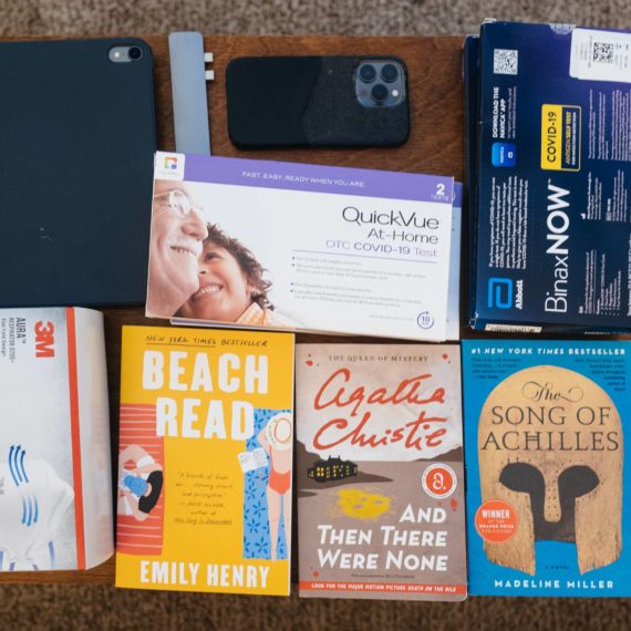 Items on a coffee table that include a tablet computer, box of N95 masks, three books, boxes of CVOID-19 tests, a few digital cameras and a mobile phone