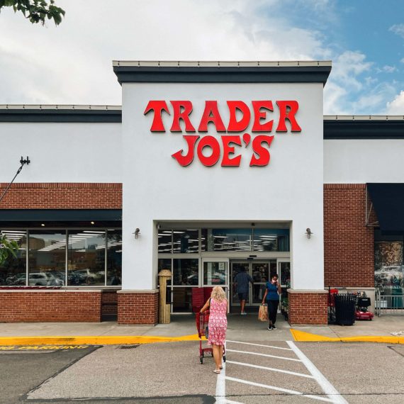 Trader Joe's entrance. A person in a pink dress approaches the entrance with a cart while a person with a mask exits the store