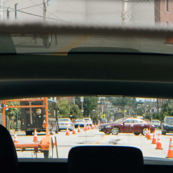 Rearview mirror showing a Nissan Altima crossing the street between orange cones