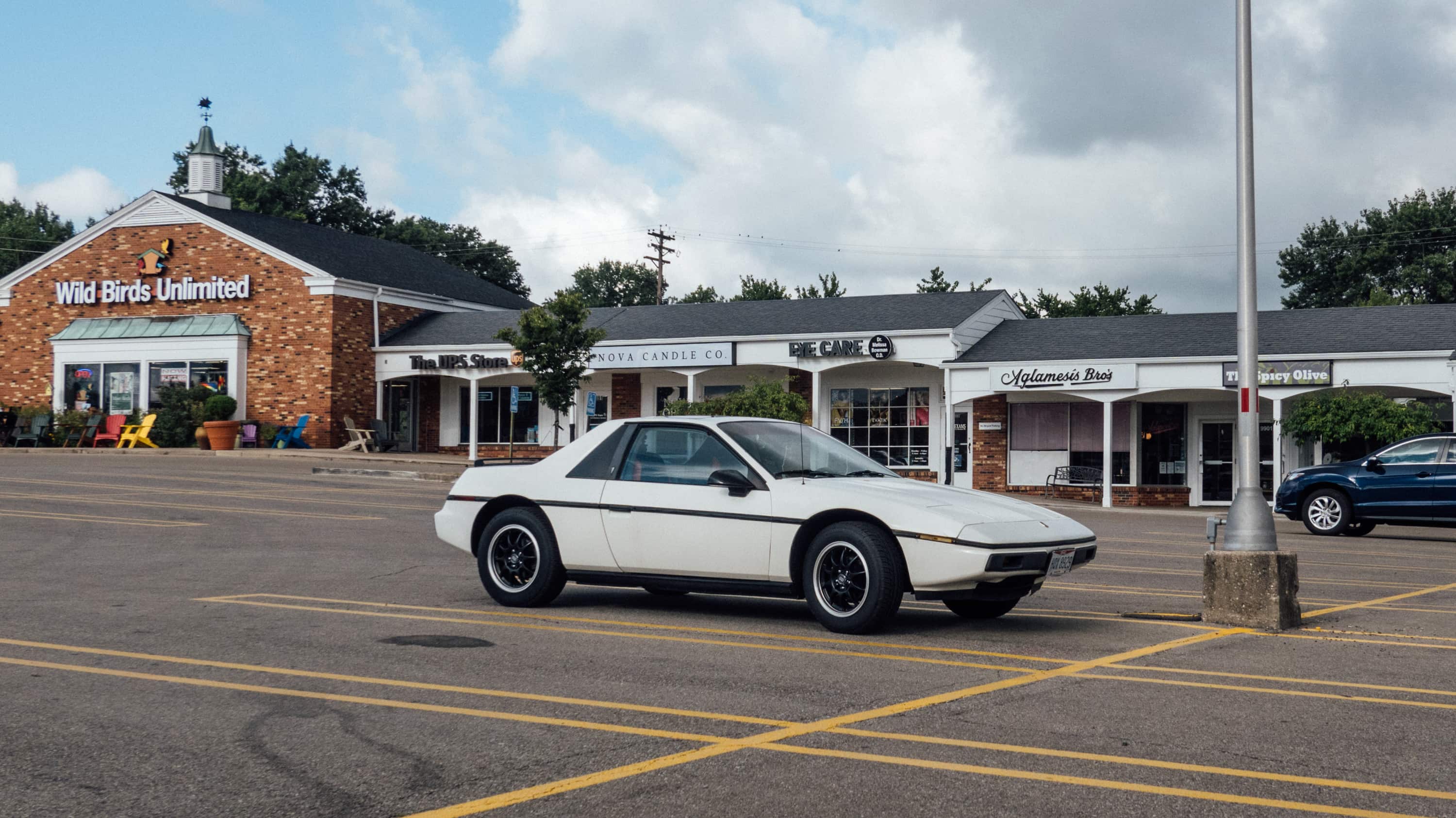 A white Pontiac Fiero from the mid-80s in pristine condition in a strip mall parking lot in the year 2022