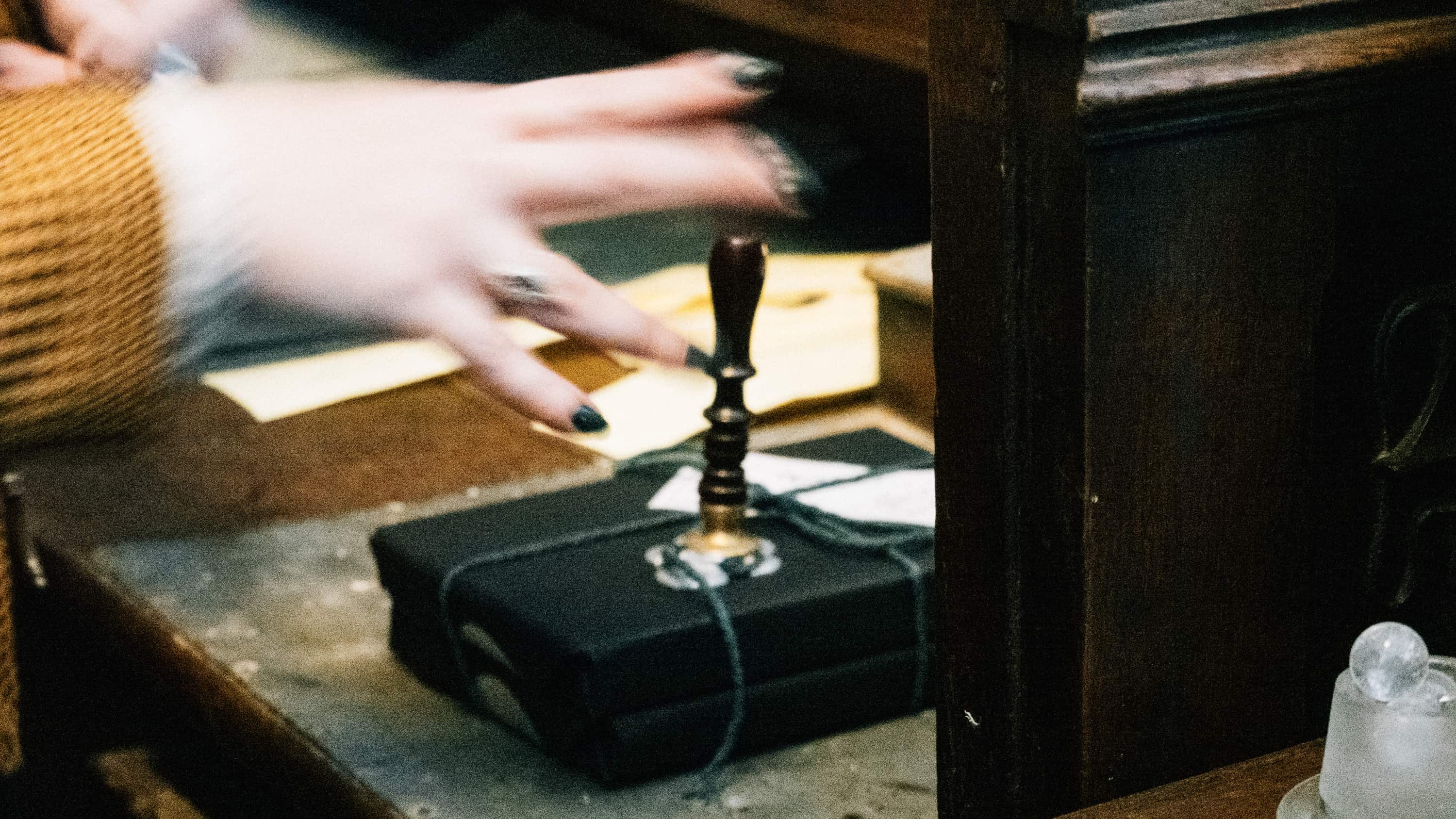 A blurry photo of hands approaching a wax seal on a package