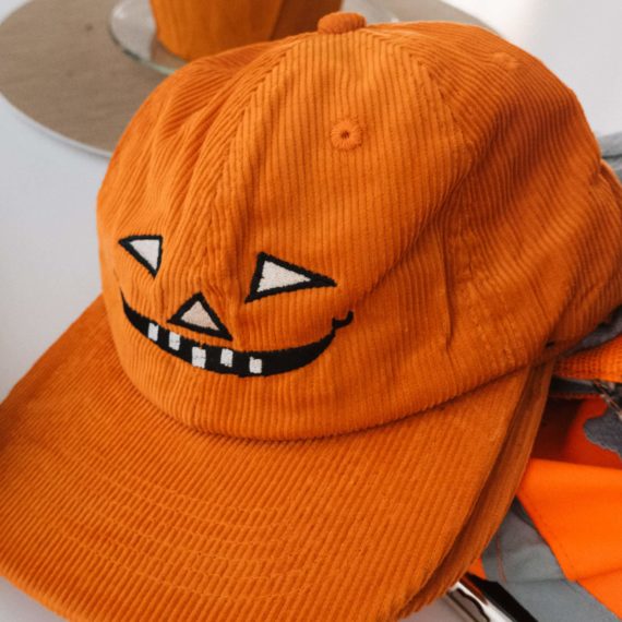 An orange corduroy hat with pumpkin carving face design