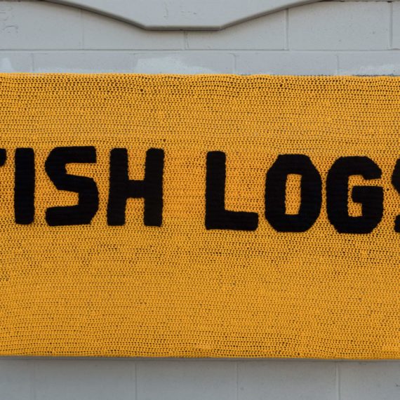 A crocheted yellow sign that reads FISH LOGS