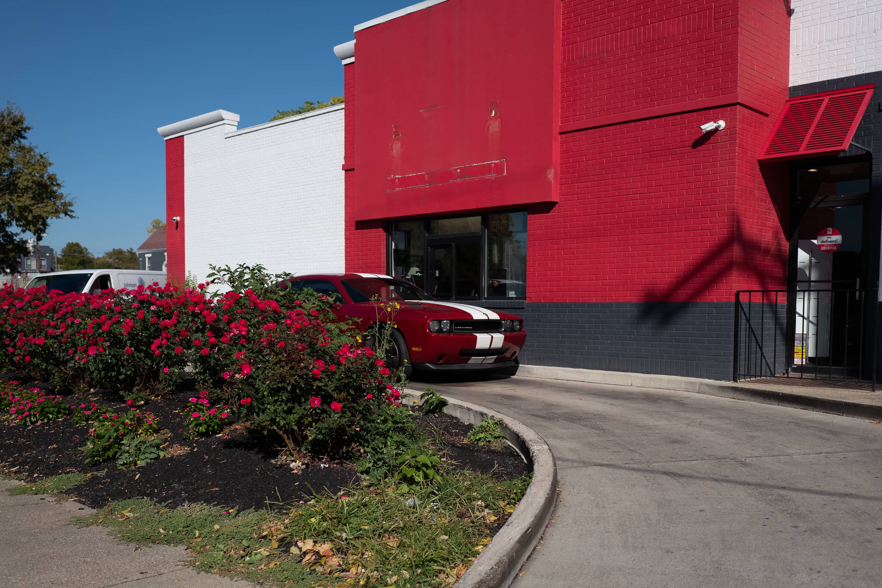 A maroon Dodge Challenger in the drive thru of a combined KFC and Taco Bell.