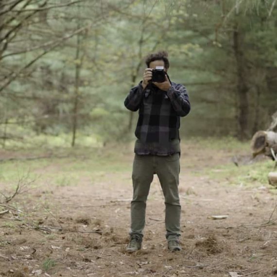 a man holds a camera in the woods