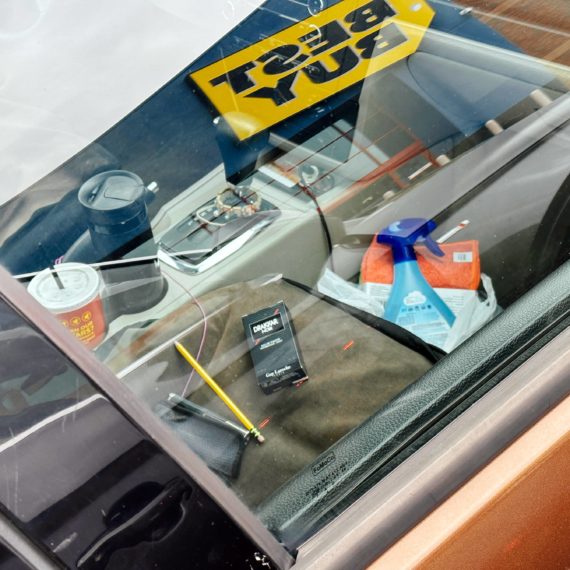 Peering inside a car that has a Febreeze bottle, pencil and box of Drakkar cologne. A Best Buy sign is reflected in the passenger window.