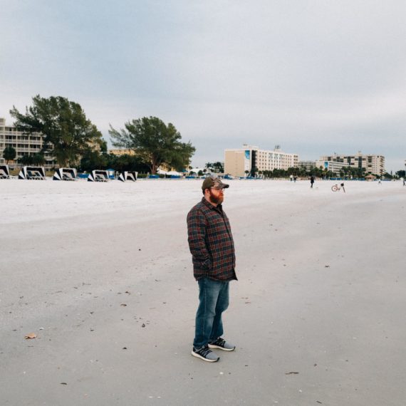 A man stands on a beach with a winter coat on