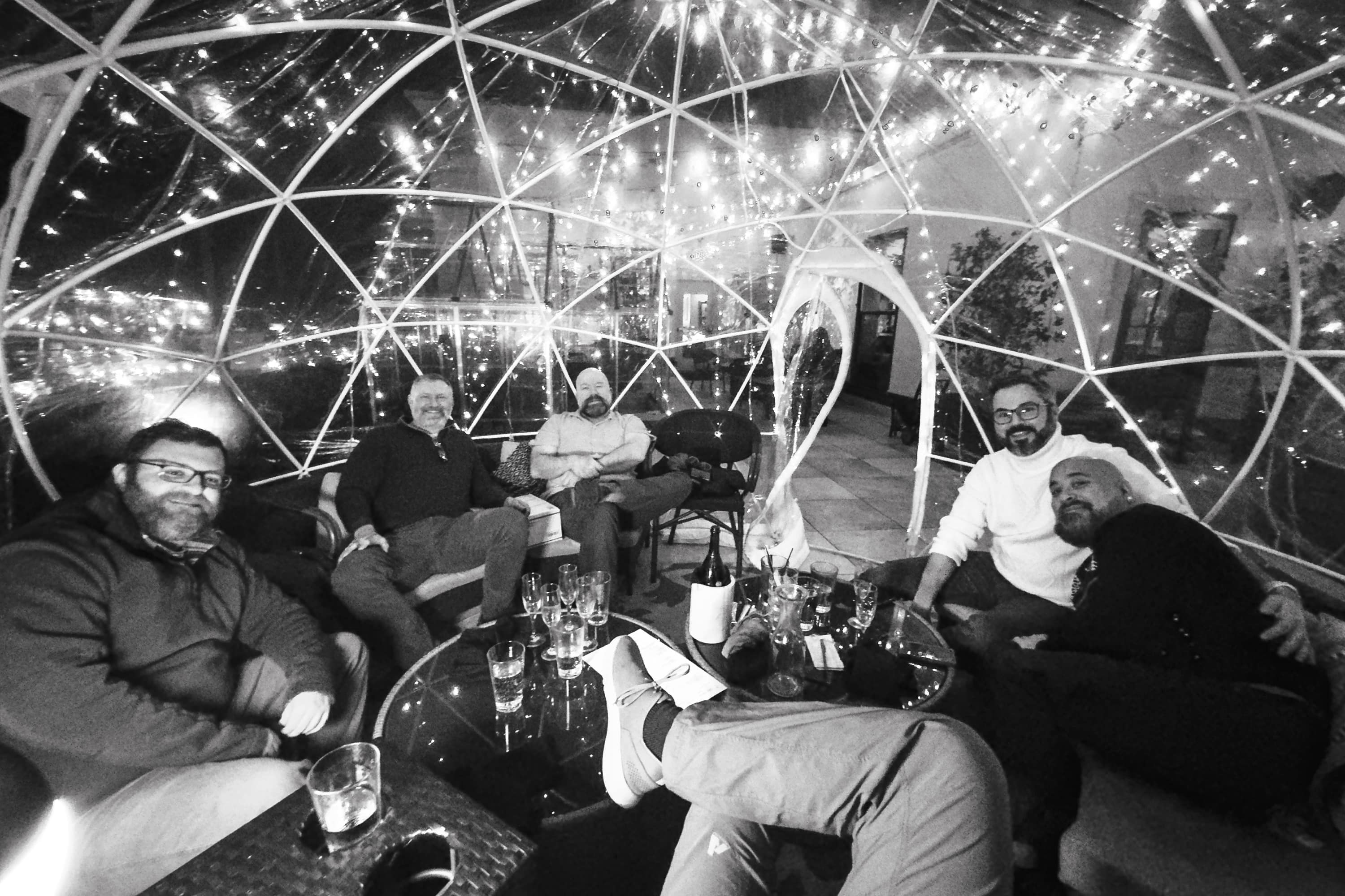 A transparent igloo set for dinner is filled with a handful of bearded men celebrating New Years Eve