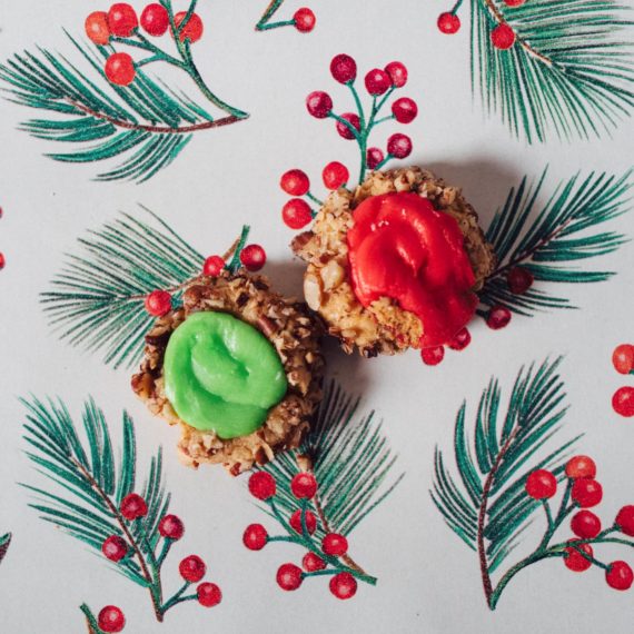 Green and Red icing on thumbprint cookies on a backdrop of wrapping paper with a holly design