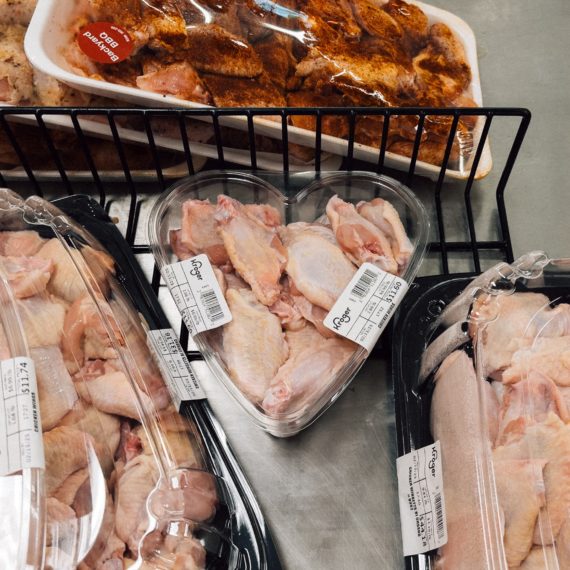 A heart shaped container filled with raw chicken wings in a cooler at a grocery store