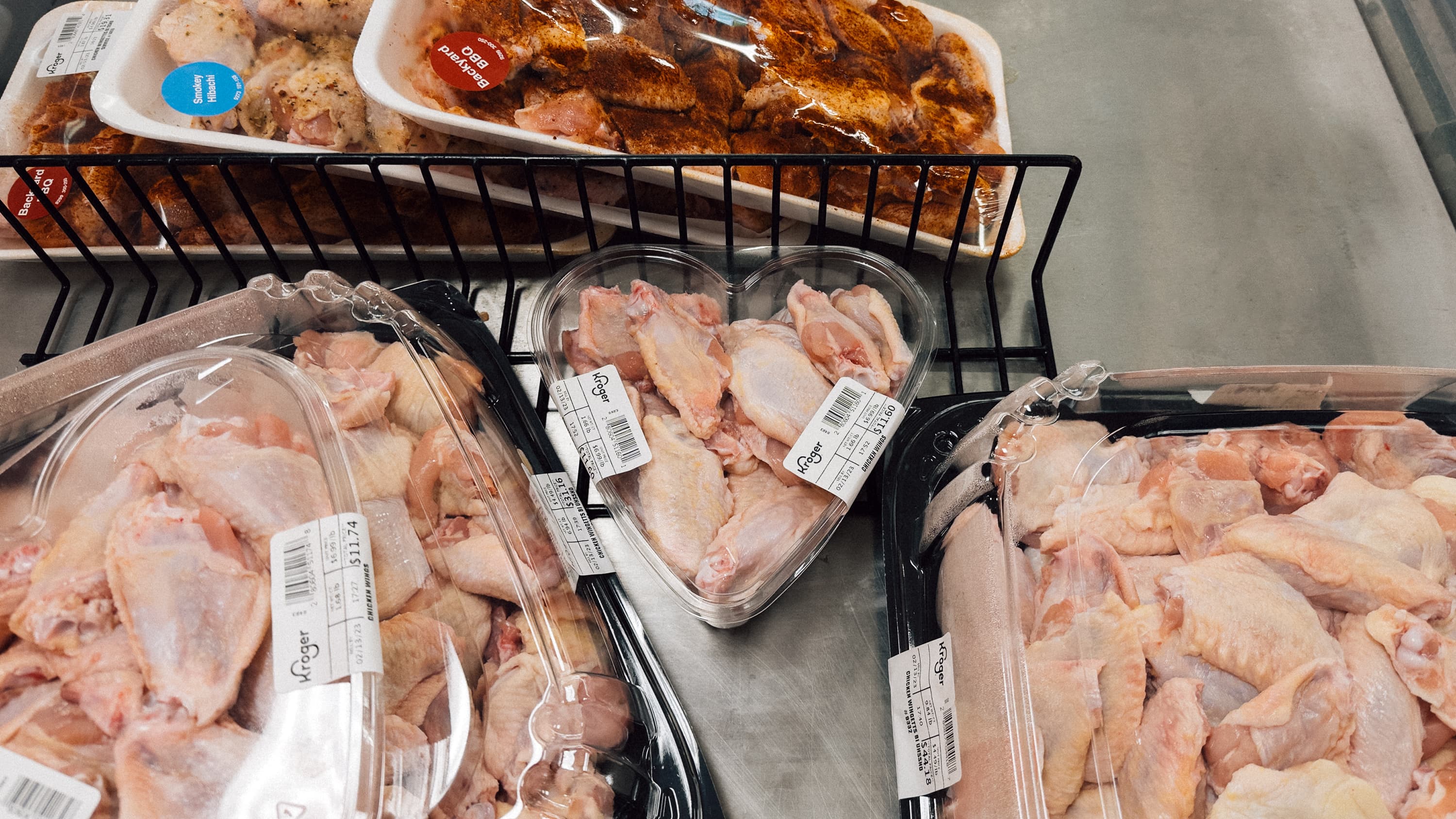 A heart shaped container filled with raw chicken wings in a cooler at a grocery store