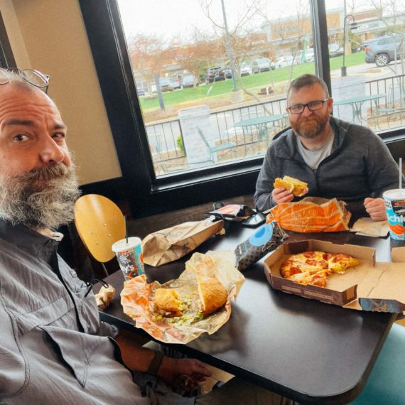 Folks eating sandwiches and a little pizza at a chain deli