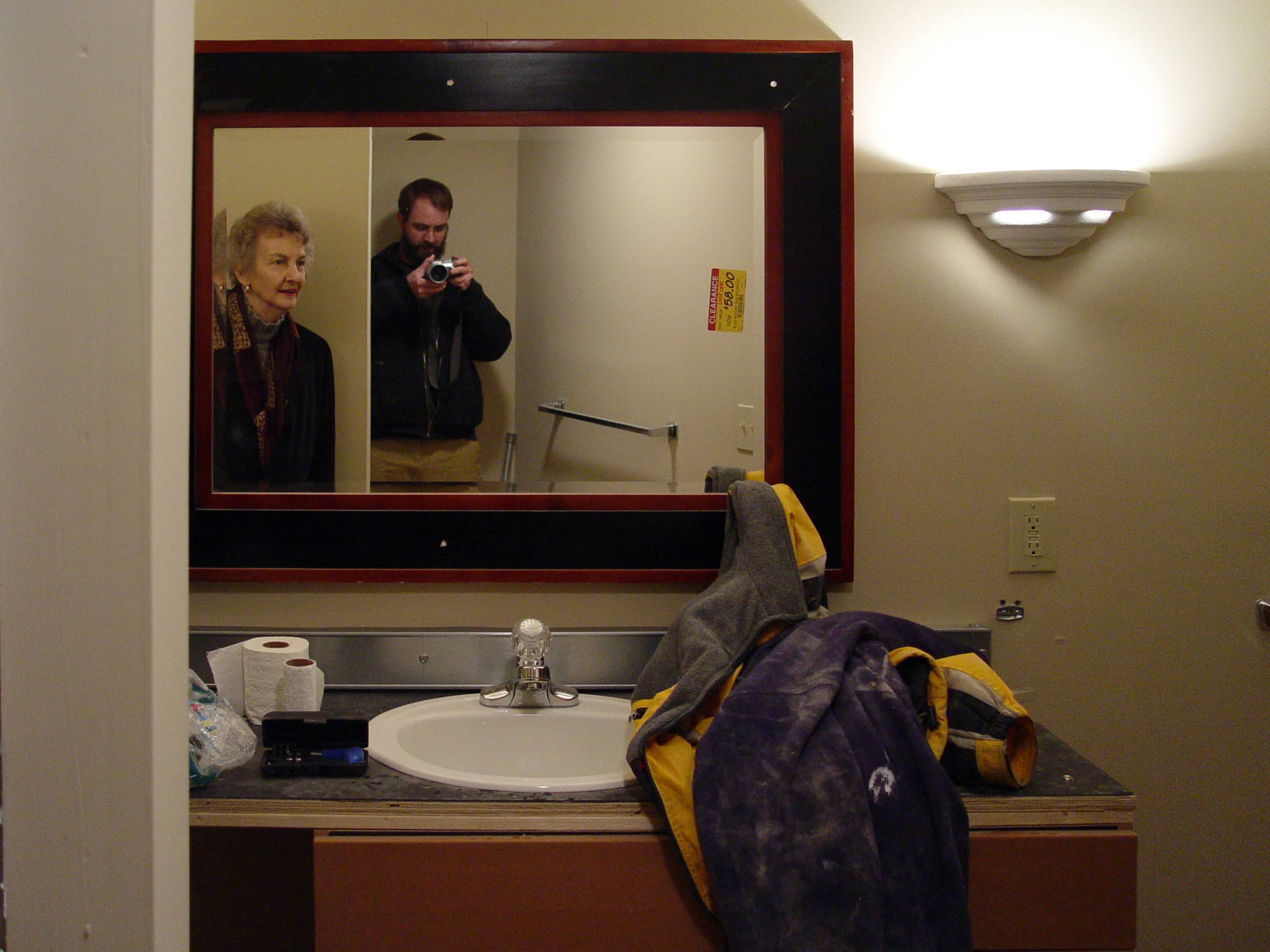 Man takes selfie in mirror with his mom walking in the frame