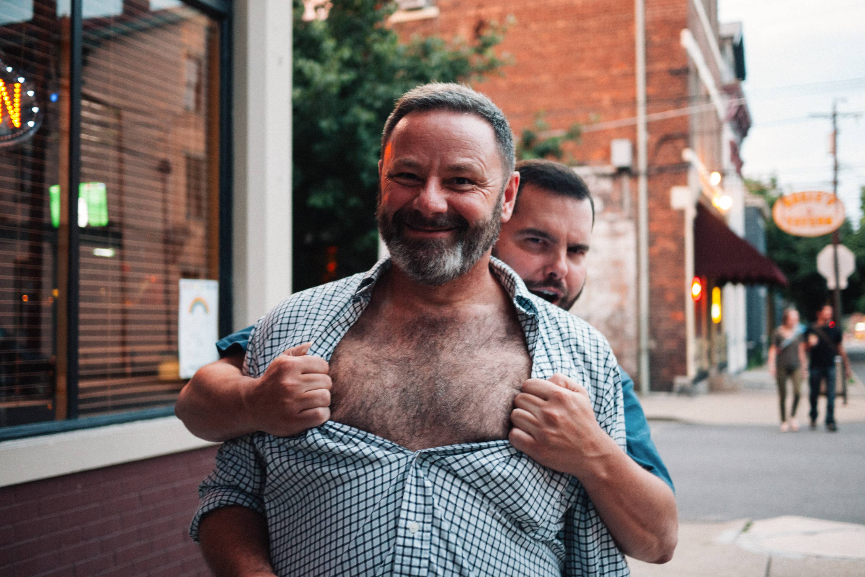 Man rips another man's shirt open revealing a hairy chest